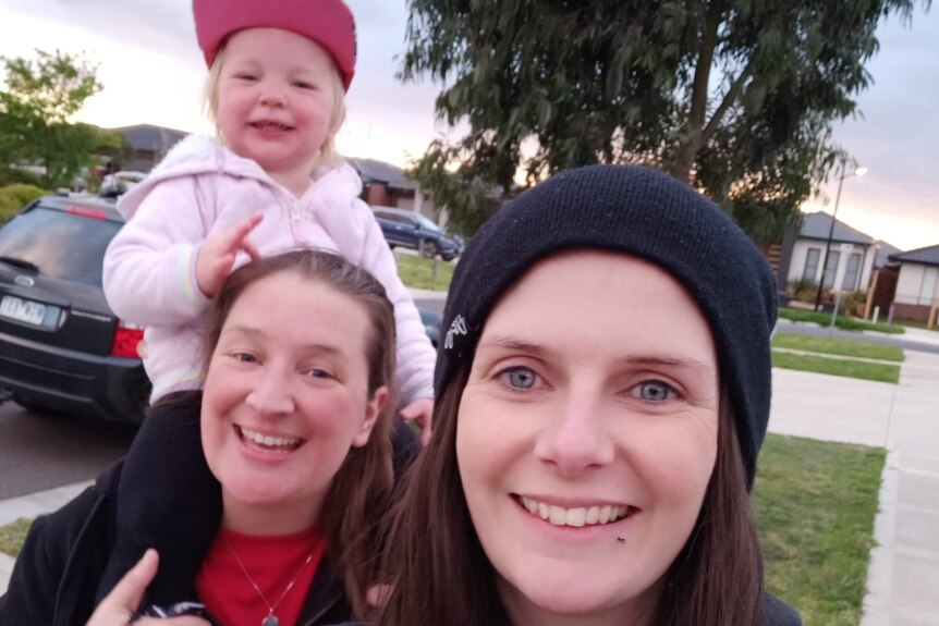 A selfie of two women, with one who has a toddler on her shoulders.
