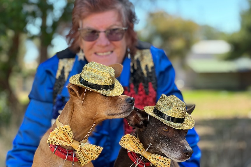 A woman brightly dressed with two small dogs wearing gold hats and bows