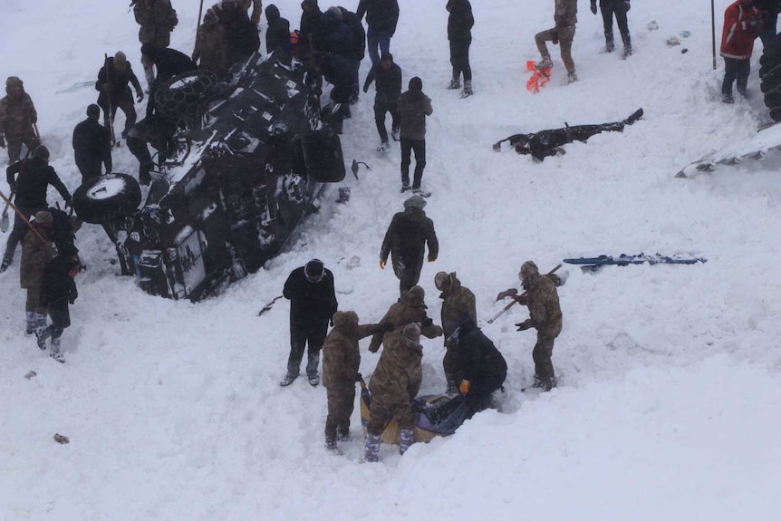 An aerial view of rescue workers gesturing and placing a person in a stretcher near an overturned vehicle.