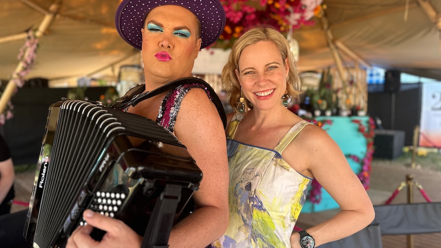man with widebrimmed purple hat and lipstick with piano accordian with woman with blonde hair smiling