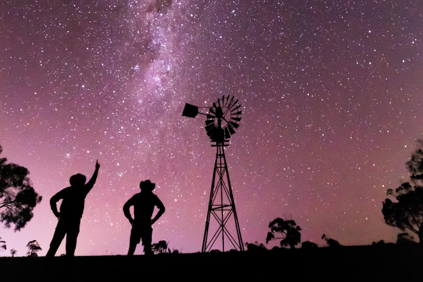 Starry Australian sky with purple tinged milky way and silhouette of farmers