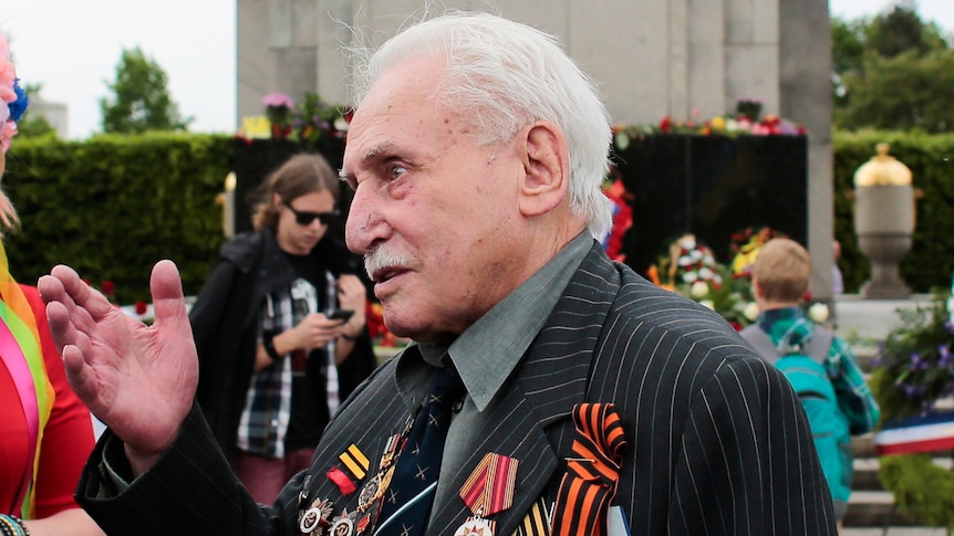 An elderly man decorated with war medals gestures.