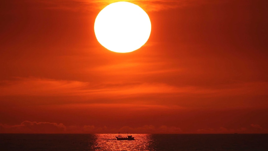 The sun rises in a brilliant orange sky over a boat on still water