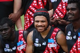 Cyril Rioli links arms with Tiwi Bombers teammates. His eyes are slightly closed but he looks happy.