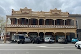 A 1800's cream and red building with latticework across the verandah, cars parked in front.