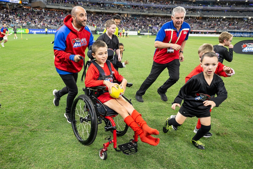 Boy in wheelchair holding football playing football with other young children on the field.