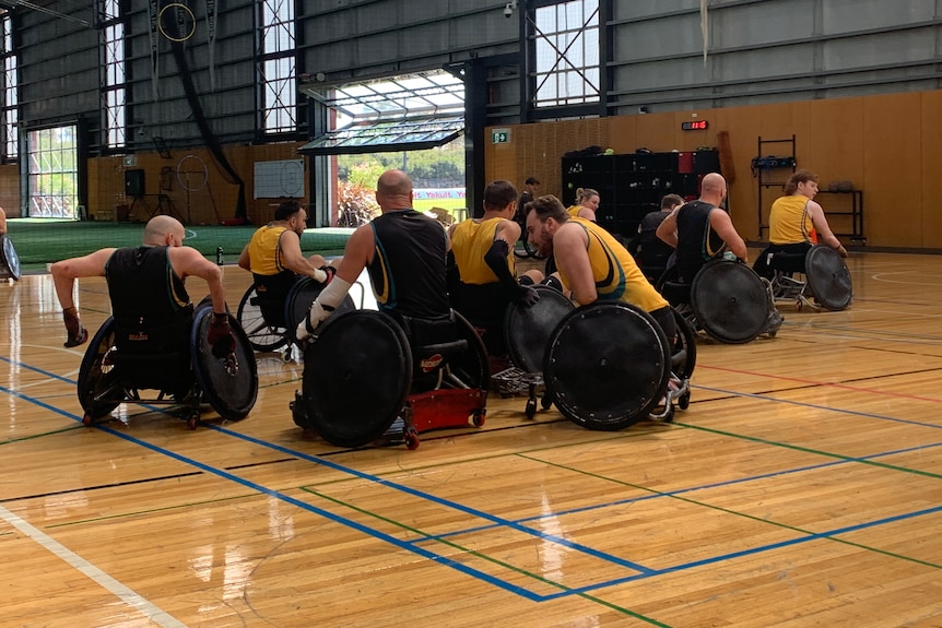 A group of wheelchair rugby players train on a court, trying to outmanoeuvre each other and set up plays.
