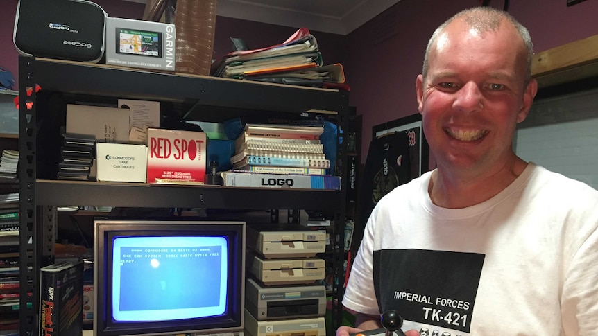 Andrew Crouch holding a gaming controller in front of the C64. He is smiling.
