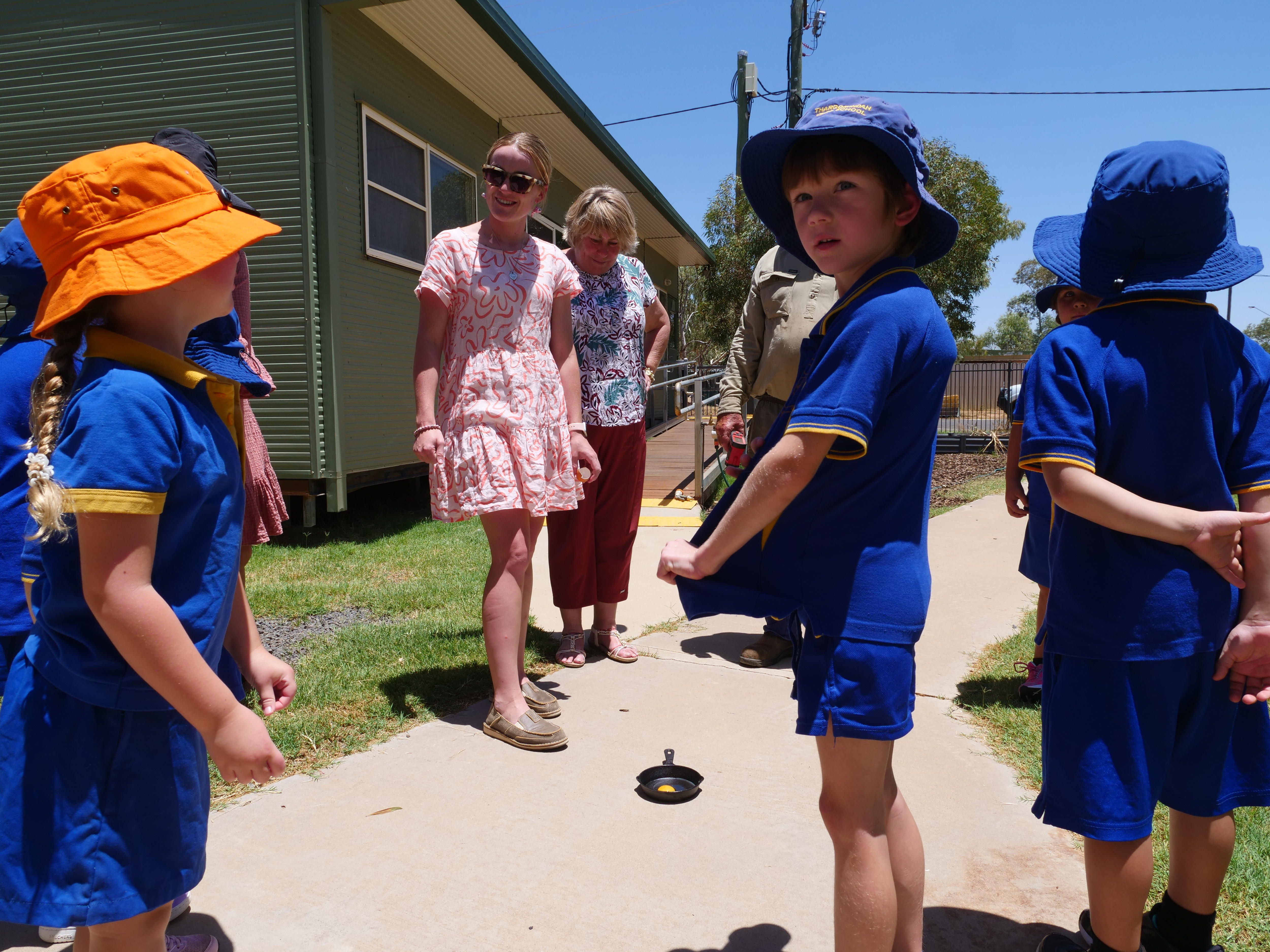 Os alunos ficam ao redor de uma pequena frigideira em uma trilha tentando cozinhar um ovo em calor extremo.