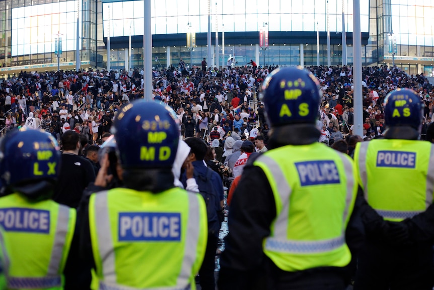 Una fila de policías en alta visibilidad mira a una multitud masiva en los escalones fuera del estadio de Wembley.