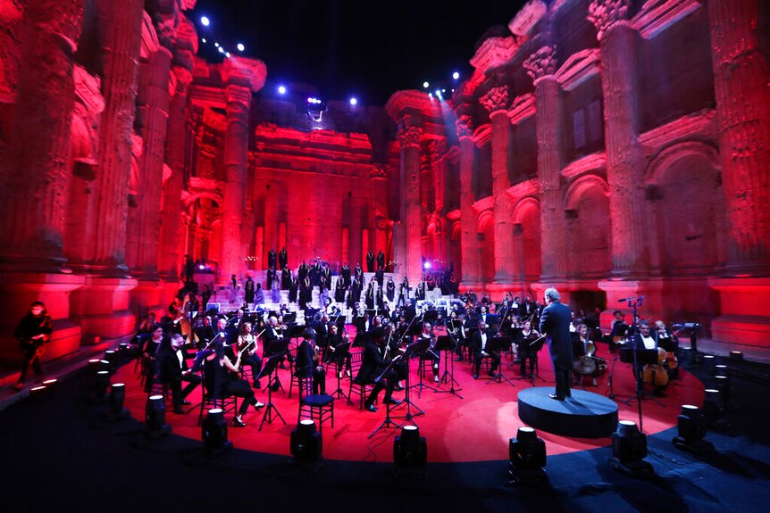 Musicians pictured inside the ancient ruins of Baalbek in Lebanon with red lighting surrounding them.