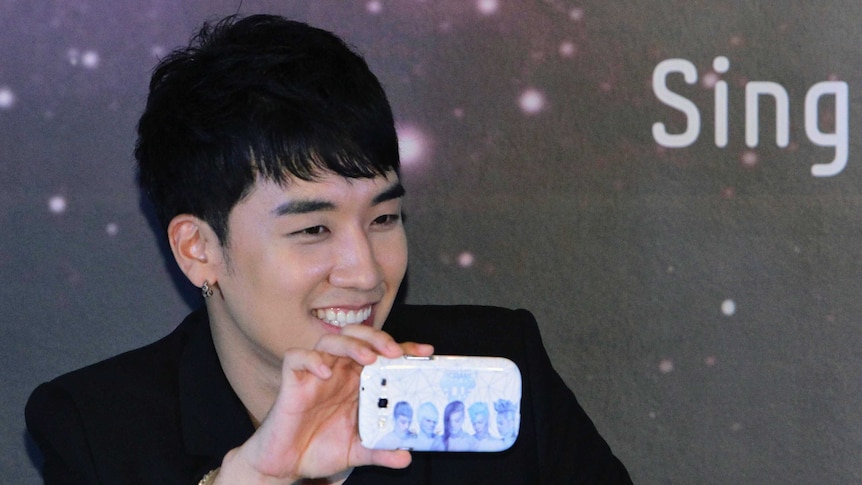 A picture of Big Bang singer Seungrri holding a phone with a cover of his band.