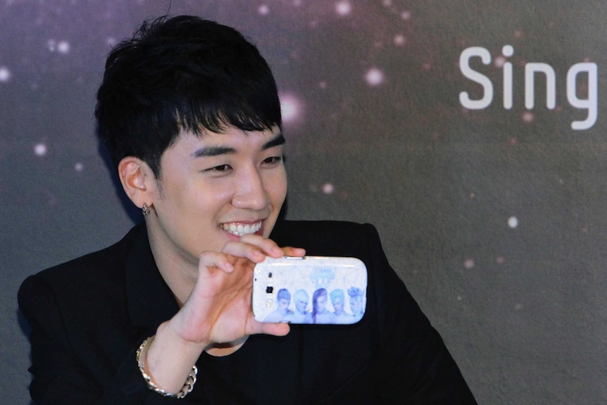 A picture of Big Bang singer Seungrri holding a phone with a cover of his band.
