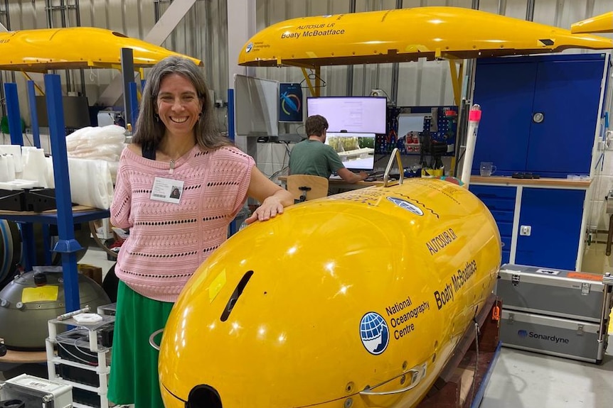 A woman stands next to a bright yellow auto submarine