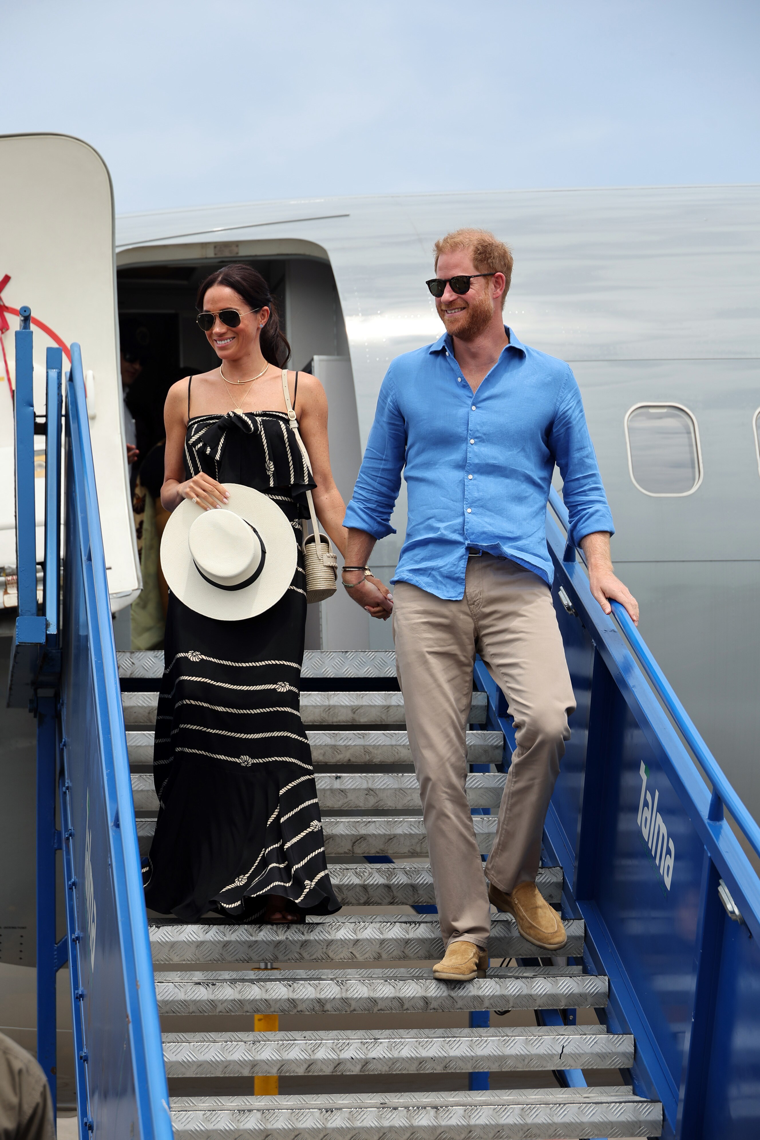 In a photo reminiscent of past royal tours, Meghan and Harry descend the steps of a plane, holding hands and smiling.