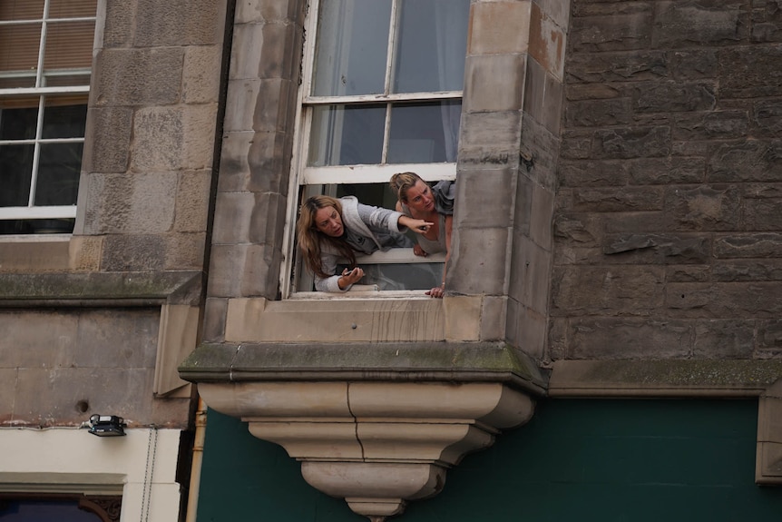 Two women lean out of their window. 