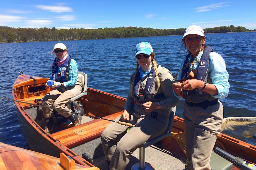 Three women on a wooden boat fly fishing