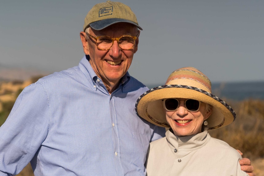 Jack Dangermond with his arm around wife Laura. Both are smiling at the camera, as they stand outside.