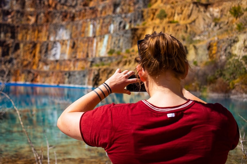 A woman stands taking a photo of the old mine pit and its stunning blue water.