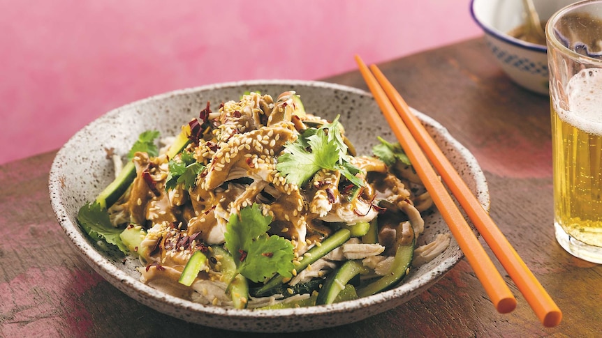 A sesame seed covered bowl of shredded chicken and salad with brown dressing on a plate with chopsticks.