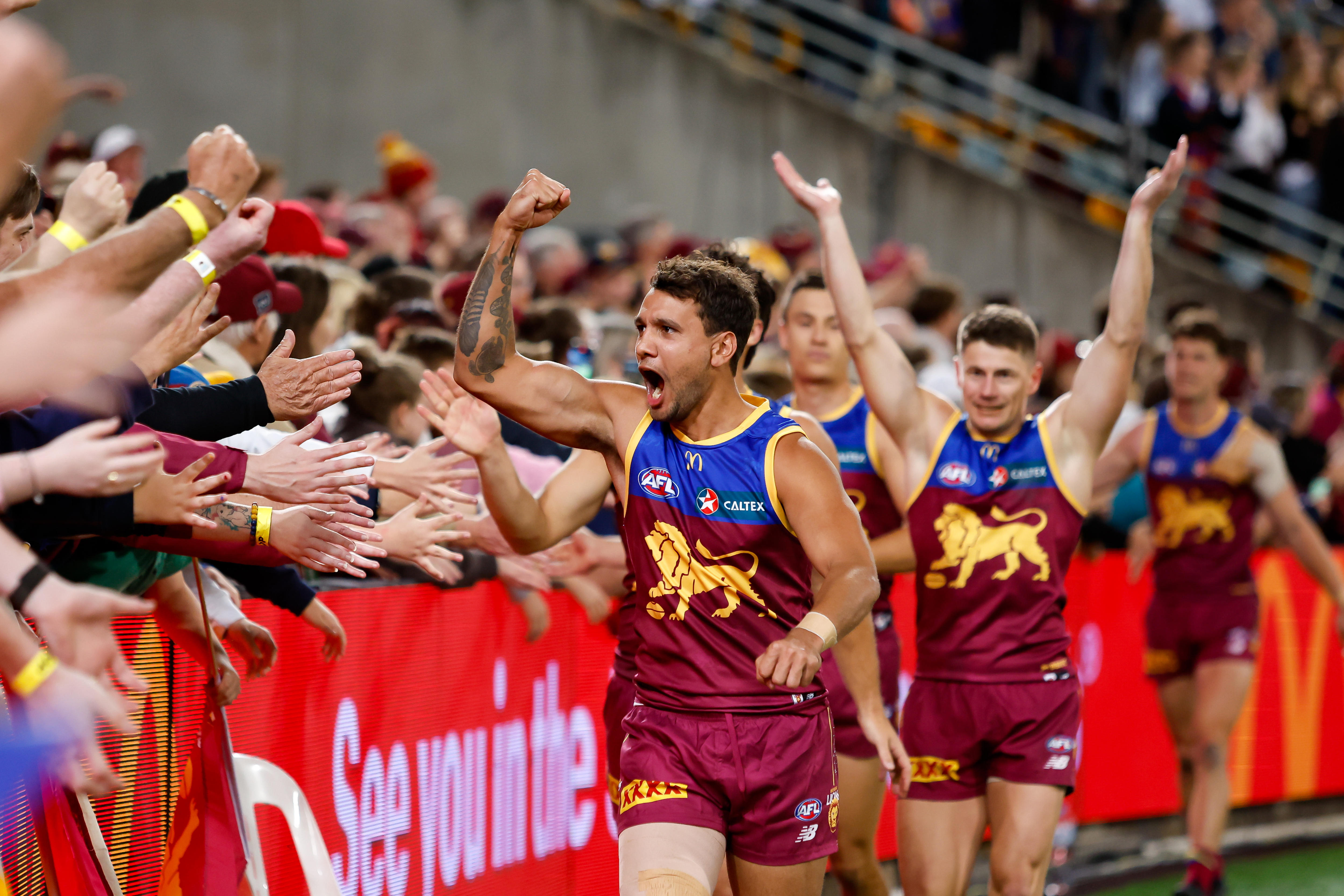 A Brisbane Lions player pumps his fist as he runs past Brisbane fans in the crowd after his team's finals win.