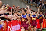A Brisbane Lions player pumps his fist as he runs past Brisbane fans in the crowd after his team's finals win.