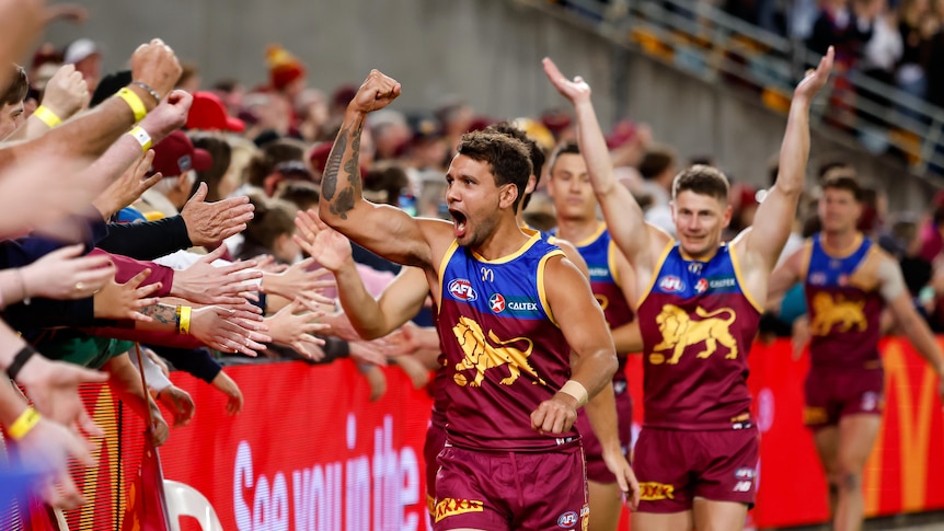A Brisbane Lions player pumps his fist as he runs past Brisbane fans in the crowd after his team's finals win.