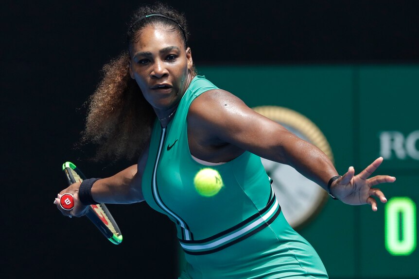 A female tennis player watches the ball with her hand behind her preparing to hit a shot