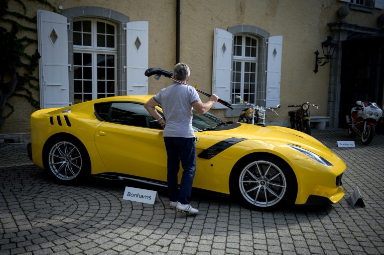 A yellow car is seen parked in behind two Bondhams signs, with a man stood in front with a golf club over his shoulder.