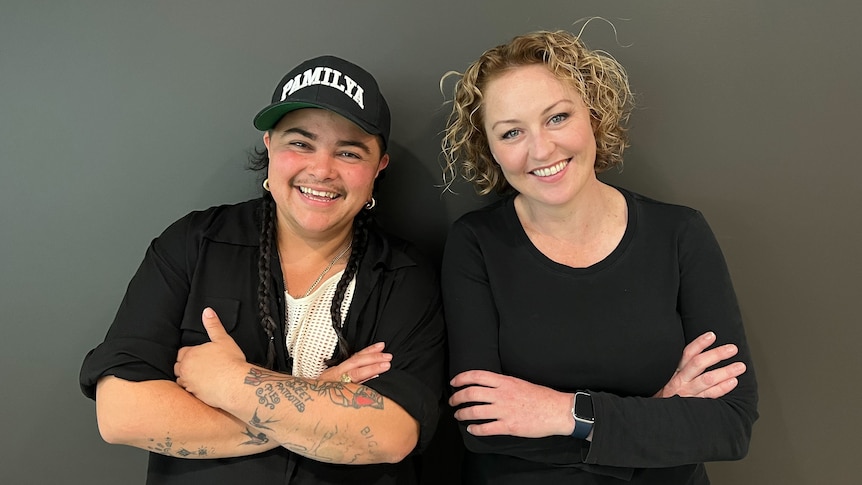 Mo'Ju and Zan Rowe stand with folded arms against a black wall