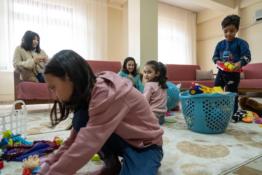 Turkish and Syrian children play with toys on the floor of a small room.