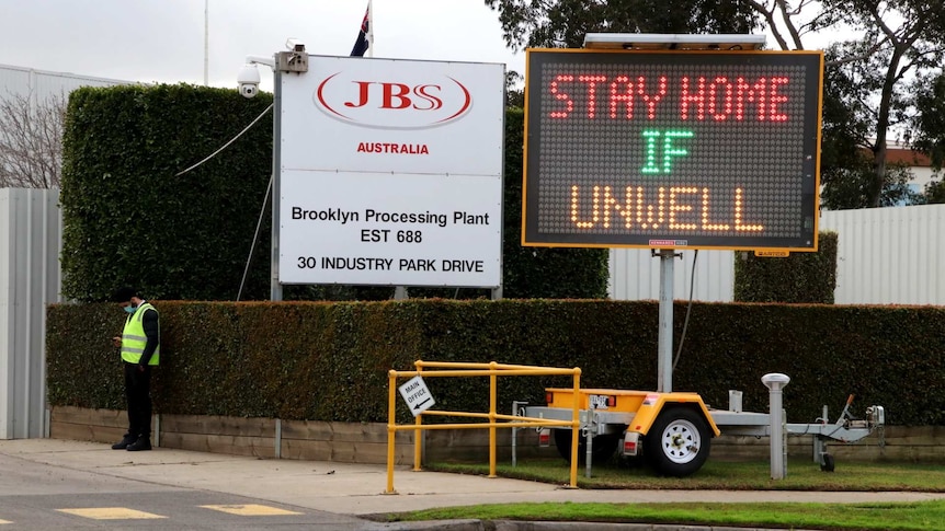 A sign outside JBS says 'stay home if unwell'.