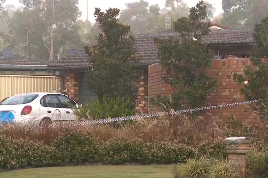 A brick home surrounded by trees, with police tape across the driveway