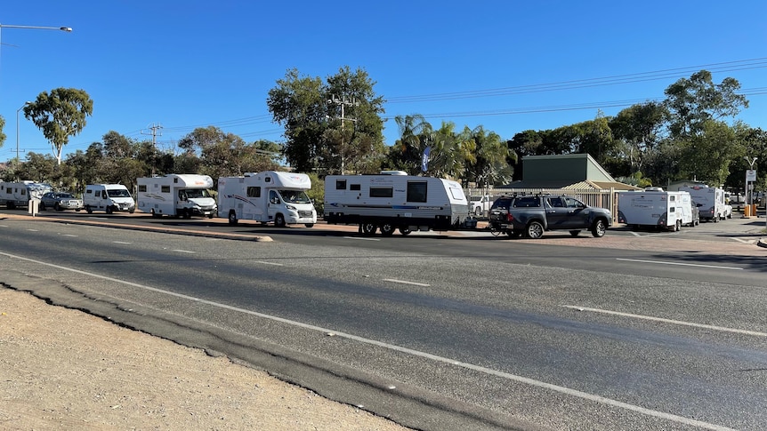 Seven caravans and campervans line up waiting to enter a caravan park in Alice Springs.
