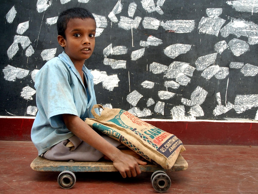 A 10-year-old Indian polio victim moves his wooden plank with wheels