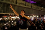 A woman holds her hand up in the air while speaking into a microphone in front of a crowd of protesters.