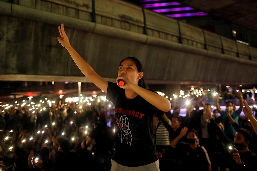 A woman holds her hand up in the air while speaking into a microphone in front of a crowd of protesters.