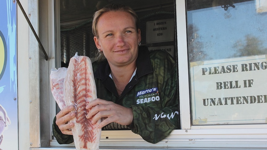 A woman holds barramundi fillets out of a fish van window