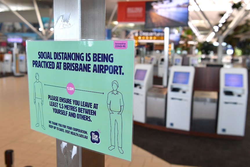 A sign encouraging social distancing near empty check-in counters at Brisbane International Airport.