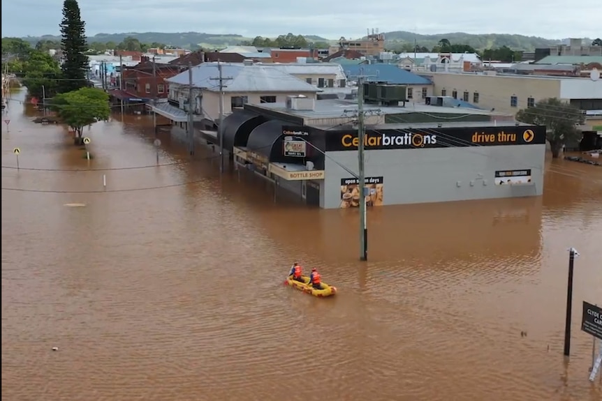 Two men kayak down a flooded street with buildings half under water