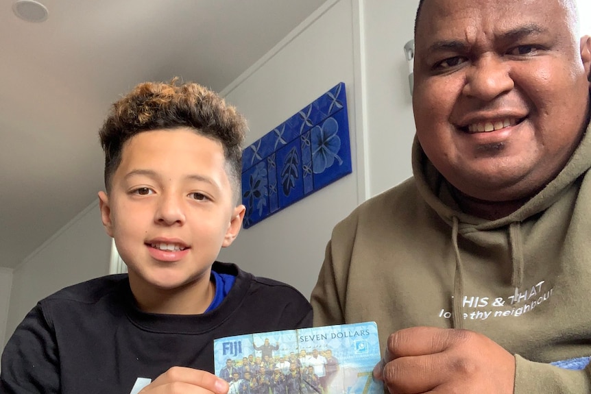 Man and young boy hold edges of note while sitting on a couch.