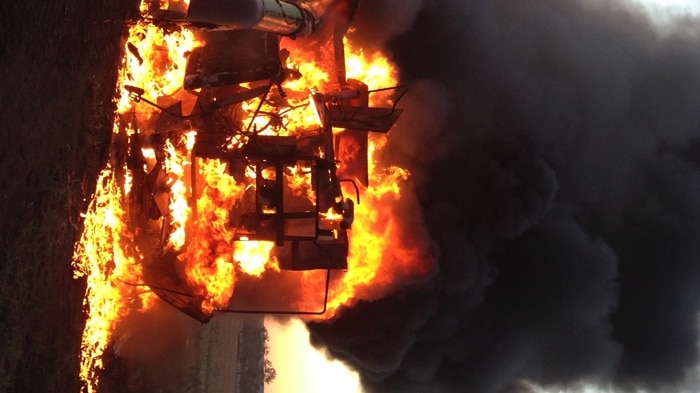 A harvesting machine burning on a Queensland property in front of a sunset.