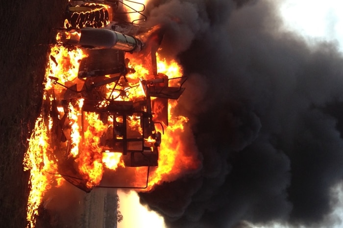 A harvesting machine burning on a Queensland property in front of a sunset.