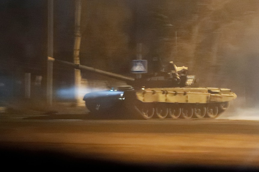 A grainy picture of a tank driving down a street at night. 