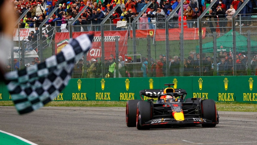 A formula one car on a race track with a checkerboard flag visible. 