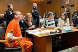James and Jennifer Crumbley sit at a table in court wearing prison clothes, awaiting sentencing