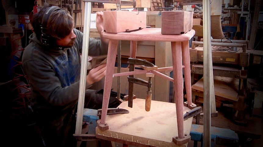 A man works on a jarrah dining chair in a workshop