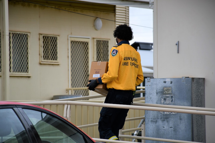 A man with a rural fire service shirt carries a box to a home.
