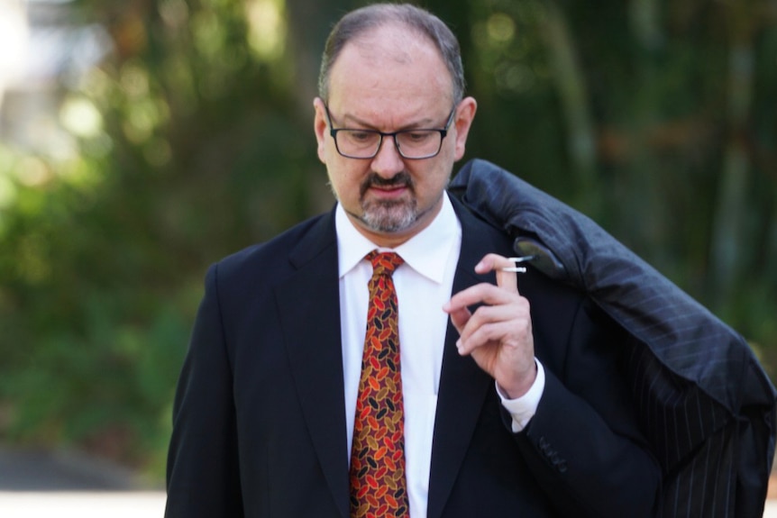 A mid shot of Paul Yovich SC walking outside the Supreme Court in Perth wearing a suit and carrying a suit bag.