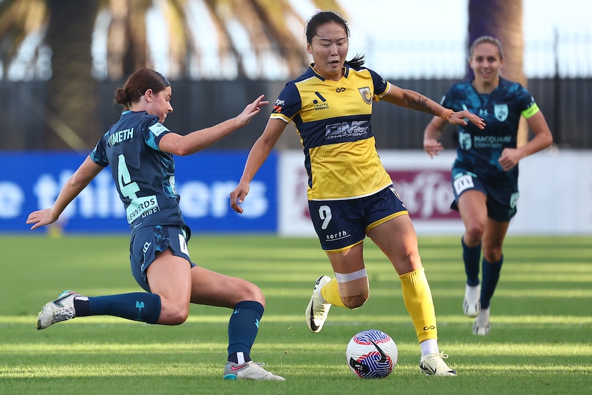 Two soccer players, one wearing dark blue and one wearing yellow and navy, challenge each other during a match